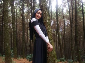 Portrait of smiling woman standing by tree in forest