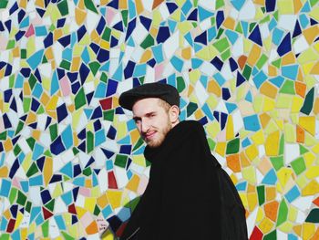 Portrait of smiling young man standing against colorful mosaic wall
