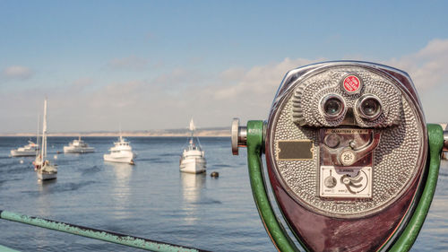 Close-up of coin-operated binoculars by sea against sky