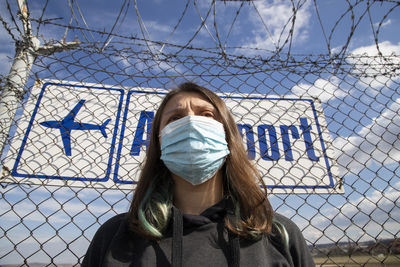 Low angle view of woman wearing mask standing against fence