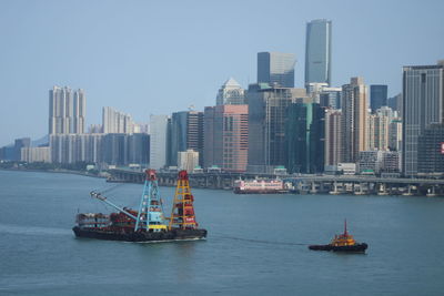 Sailboats in sea against modern buildings in city