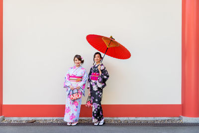 Portrait of woman with red umbrella standing against wall