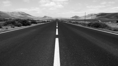 Empty road by mountains against sky