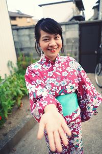 Portrait of smiling young woman wearing kimono gesturing outdoors