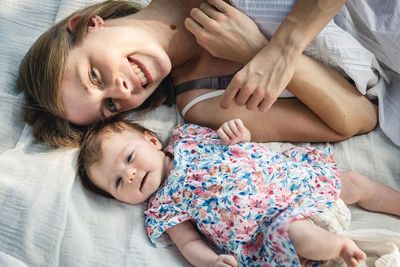 High angle portrait of mother lying with toddler daughter on bed