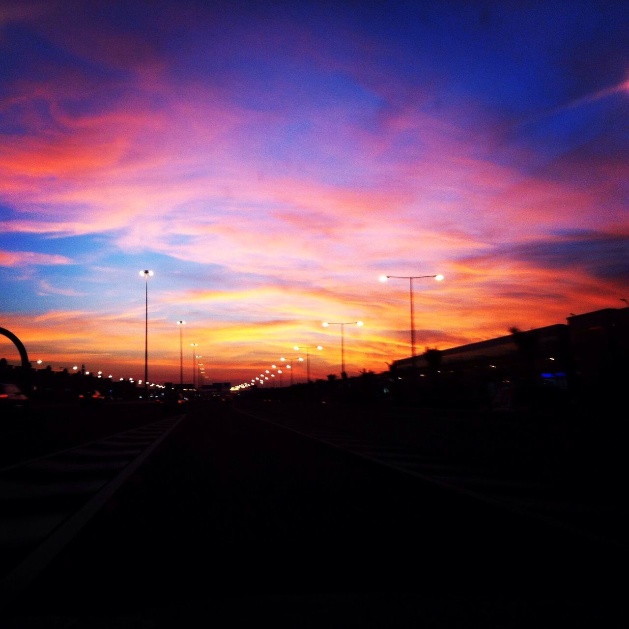 sunset, transportation, sky, silhouette, road, the way forward, cloud - sky, street light, orange color, road marking, car, diminishing perspective, street, dusk, cloud, mode of transport, dramatic sky, land vehicle, empty, vanishing point