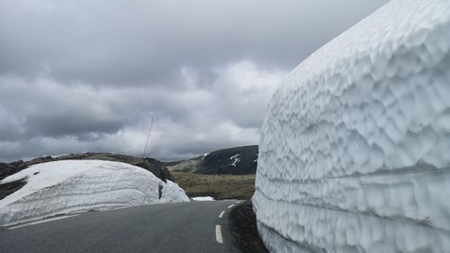 Road by snow covered landscape against sky