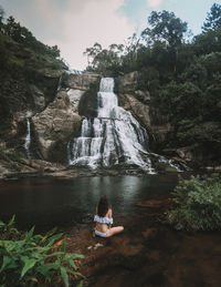 Woman sitting on rock by waterfall