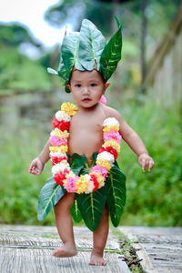 Portrait of cute boy wearing leaves and garland standing outdoors