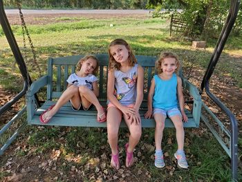 Portrait of sisters sitting on swing at park