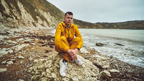 Full length portrait of young man sitting on rock at beach