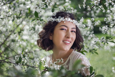 Portrait of a young beautiful woman in white clothes standing next to blooming cherry tree in spring