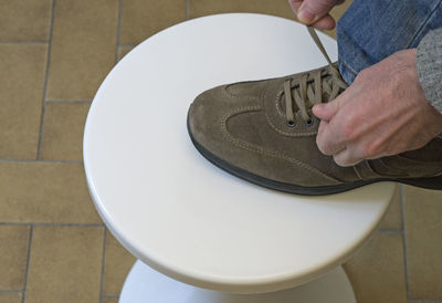 Low section of man tying shoelace on stool at home