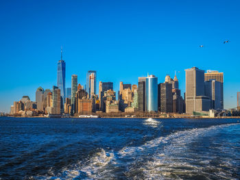 Sea by modern buildings against clear blue sky