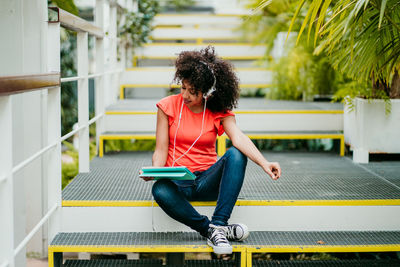 Woman with curly hair watching video over digital tablet while sitting on steps