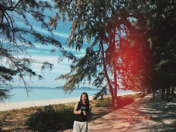 Portrait of woman standing by tree against sky