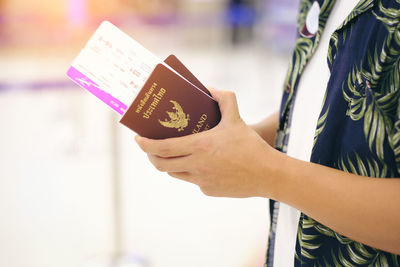 Midsection of man holding passport and tickets at airport