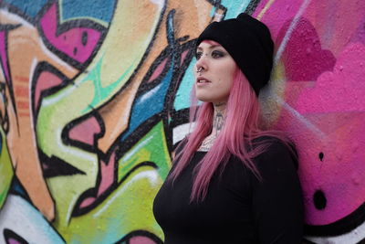 Young woman with pink hair standing against graffiti wall