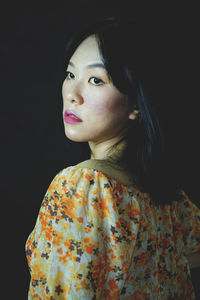 Portrait of young woman looking away against black background