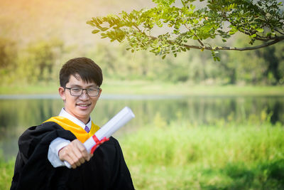 Portrait of young man in graduation gown standing at lakeshore