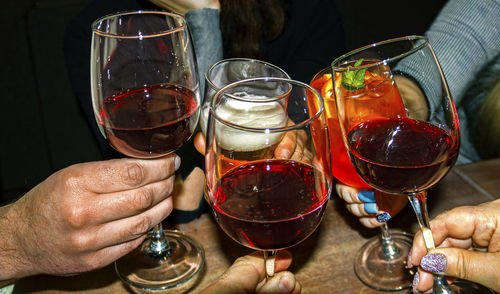 Glasses with different drinks in hands close-up on a dark background