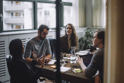 Male and female colleagues listening to businesswoman discussing ideas sitting at conference table