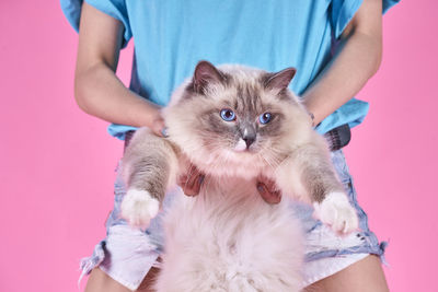 Portrait of woman holding cat against pink background
