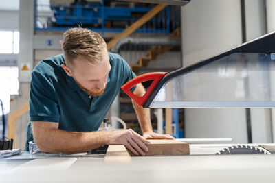Carpenter cutting plank on circular saw in production hall