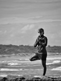 Portrait of young woman standing at beach against sky