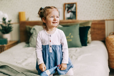 A smiling girl is sitting on a bed in a room decorated for christmas and new year