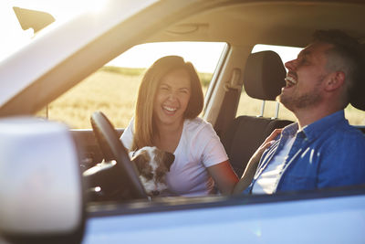 Smiling couple with dog sitting in car
