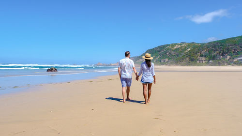 Rear view of woman walking at beach against sky