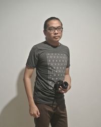Portrait of man holding digital camera while standing against wall