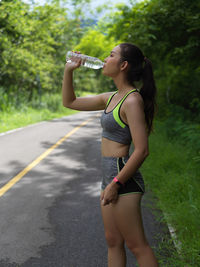 Young woman drinking water while standing by road