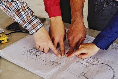 High angle view of colleagues pointing at blueprint on desk