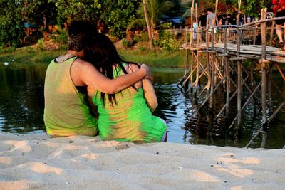 Rear view of couple sitting on sand at riverbank