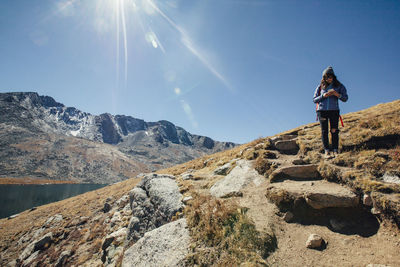 Female hiker using mobile phone while standing on mountain against blue sky