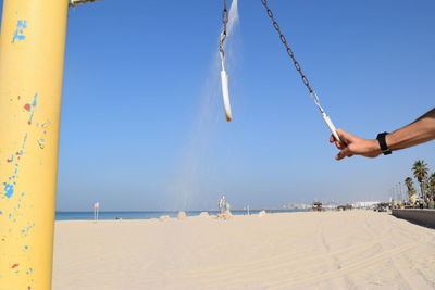 Man taking a shower on beach against clear blue sky 