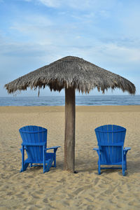 Blue beach chairs under thatched umbrella on beach sand baja mexico 
