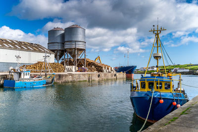 Fishing boats moored at harbor against sky