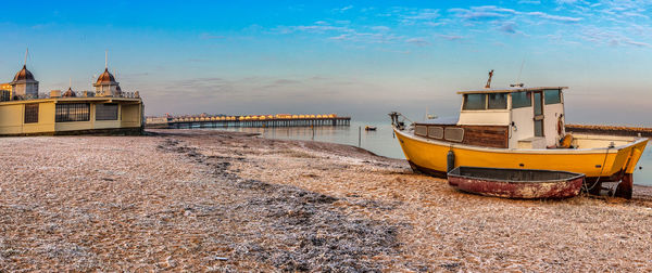 Boat moored on beach by building against sky