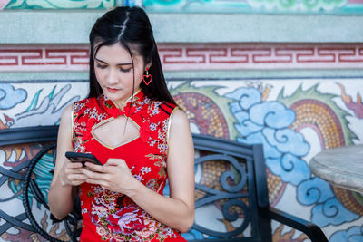 Young woman using mobile phone against wall