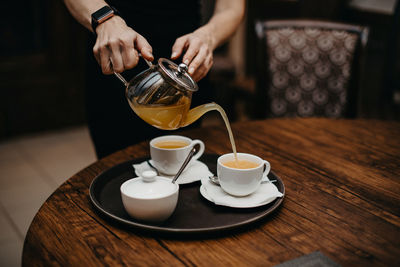 Herbal tea in a glass teapot. the girl pours a hot drink from a kettle into white ceramic cups