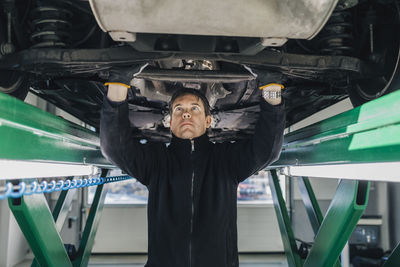 Male mechanic examining car on hydraulic lift in auto repair shop