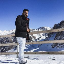 Young man standing on snowcapped mountain against clear sky