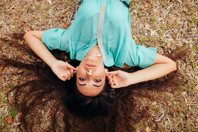High angle portrait of woman listening music on headphones while lying on grassy field