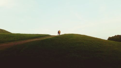 Boys standing on grassy field against clear sky at burial mound