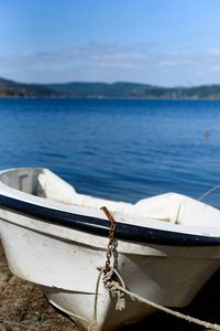 Rope tied to boat moored at shore against blue sky