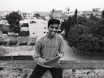 Portrait of smiling young man sitting on retaining wall