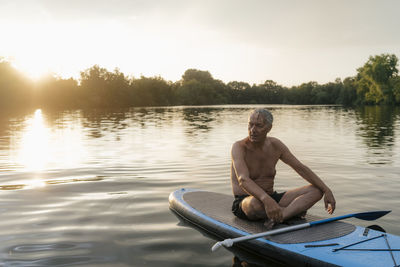 Senior man sitting on sup board at sunset